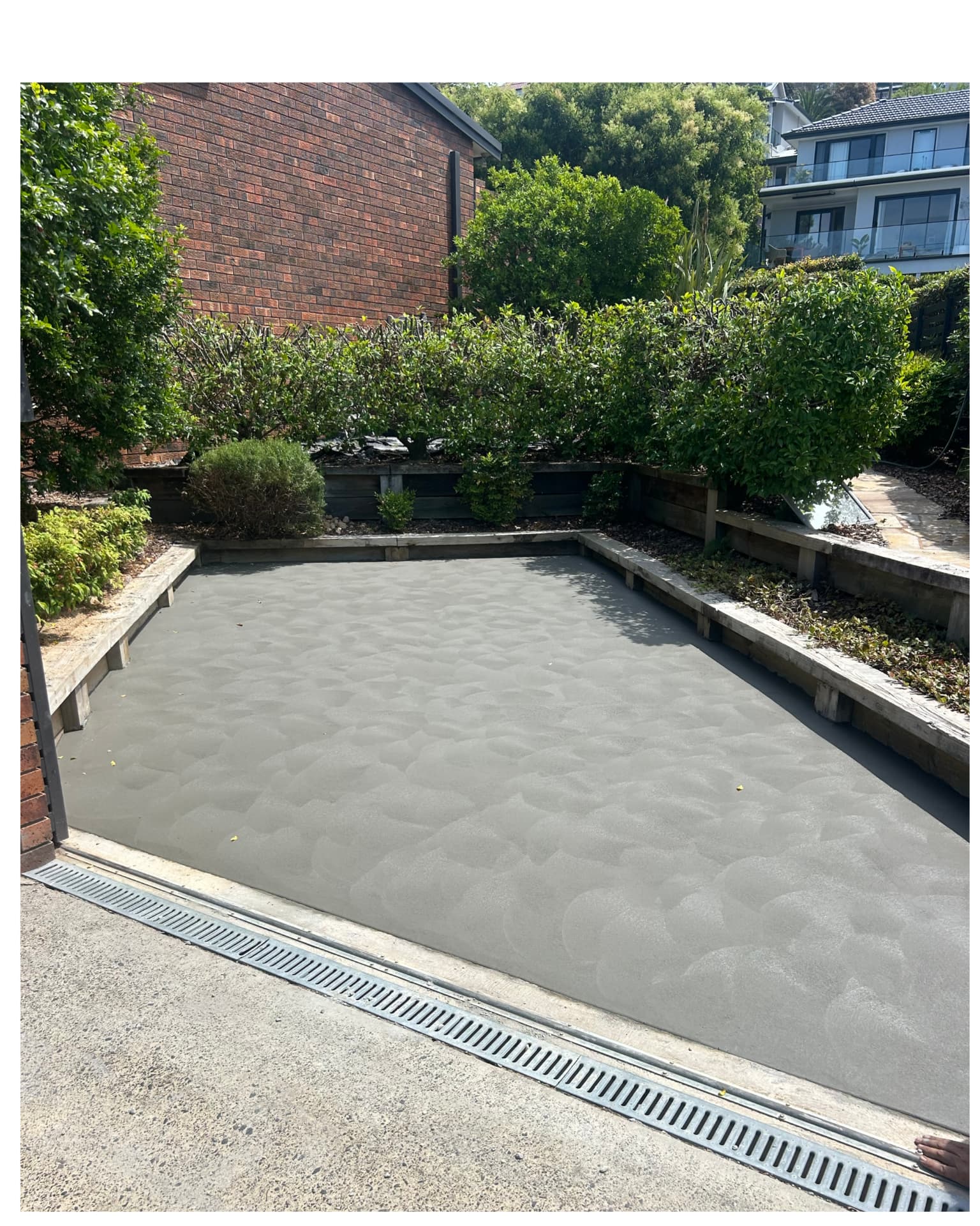 Freshly poured concrete driveway with strip drain between garden retaining walls